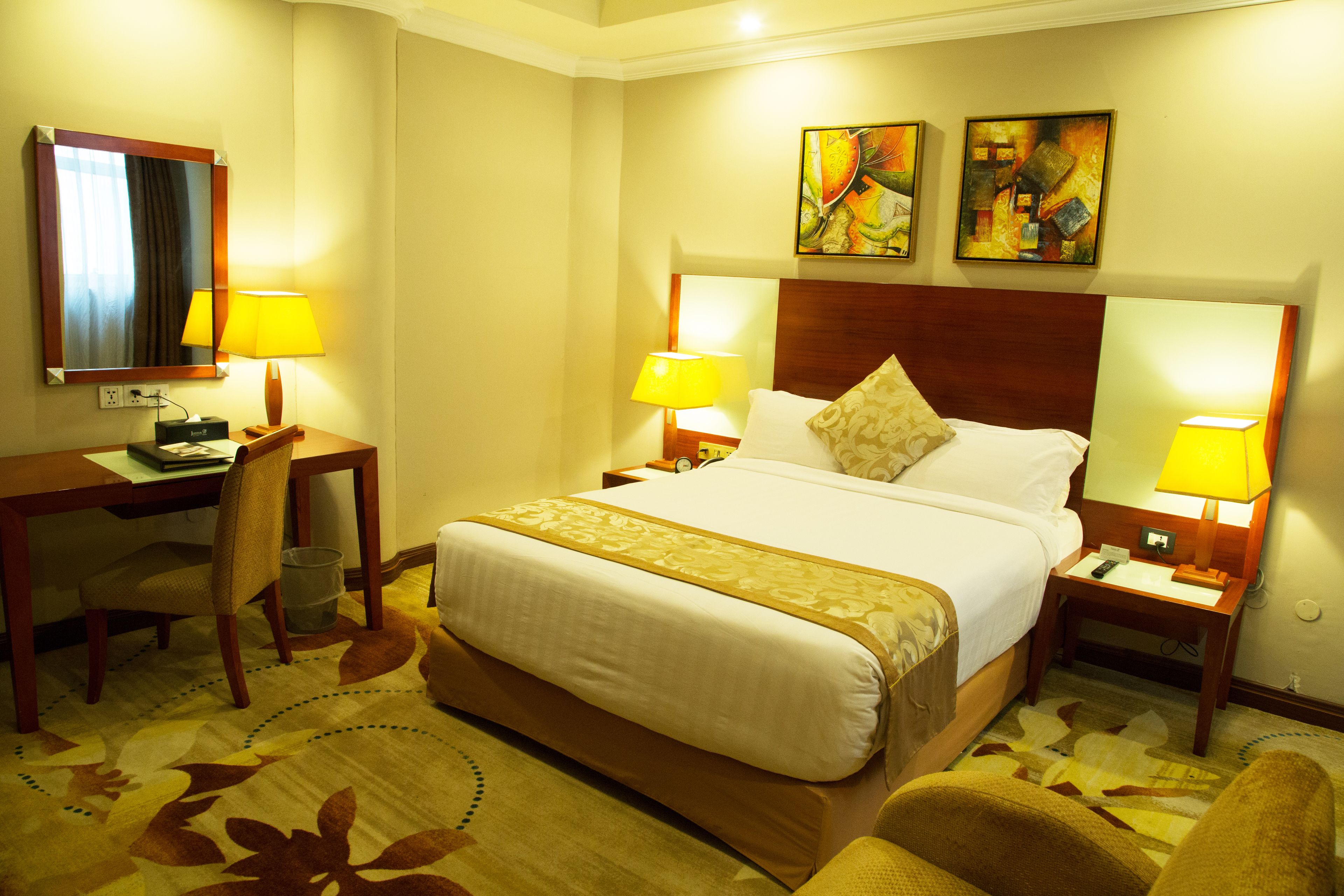 A hotel room with a large bed, two bedside tables with lamps, a desk with a chair, and a mirror.