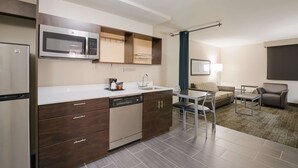 A compact kitchen with a microwave, dishwasher, and a small sink. There is a dining area with a table and chairs, and a sofa. - Best Western Northwest Indiana Inn (Hammond)