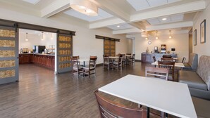 A spacious dining area with wooden flooring, tables, and chairs. There is a kitchen area in the background with a bar and counter. - Best Western Northwest Indiana Inn (Hammond)