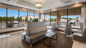 A spacious lobby with a modern design, featuring a large seating area with a sofa and armchairs, a coffee table, and large windows offering a view of the parking lot and surrounding buildings. - Best Western Northwest Indiana Inn (Hammond)