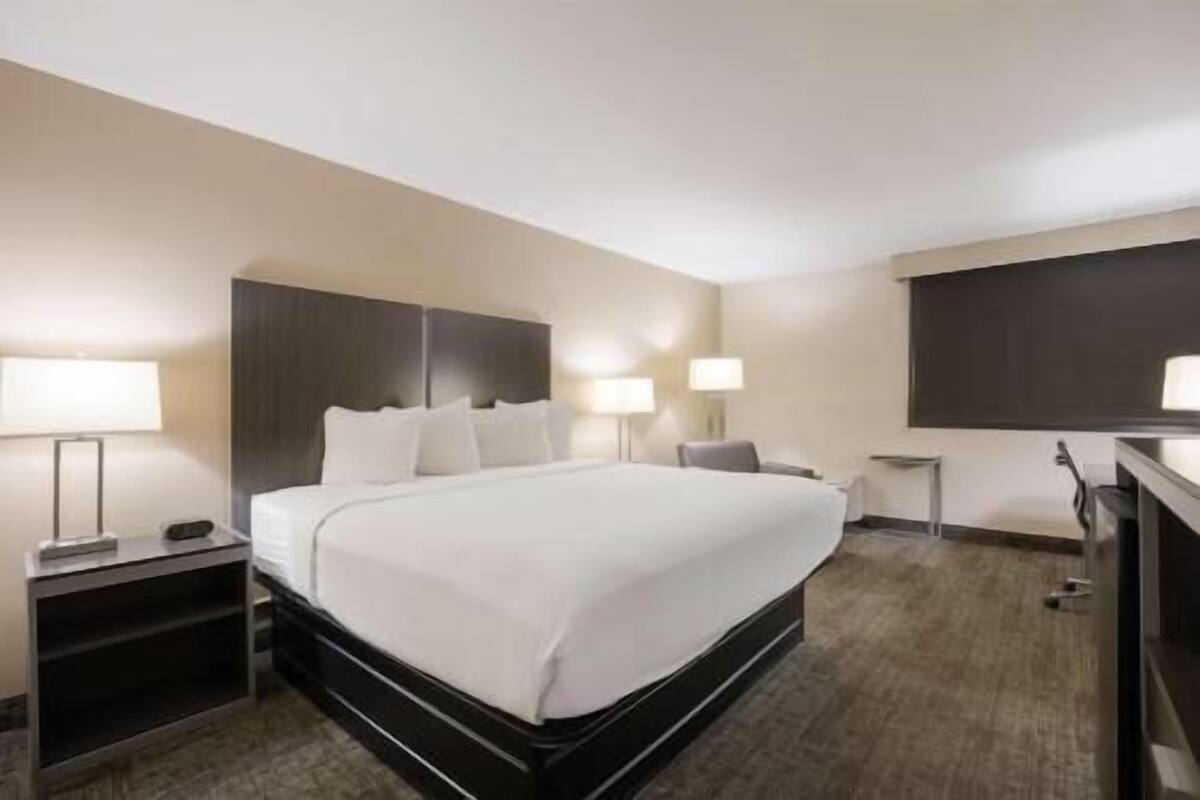 Ein Hotelzimmer mit einem großen Bett, zwei Nachttischen mit Lampen, einem an der Wand montierten Flachbildfernseher und einem Teppichboden.