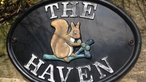 A black metal sign with a squirrel holding a branch and the words "THE HAVEN" in white letters. - The Haven (Morpeth)