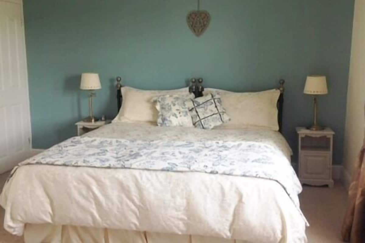 A bedroom with a bed, two bedside tables, and a wall-mounted light fixture.