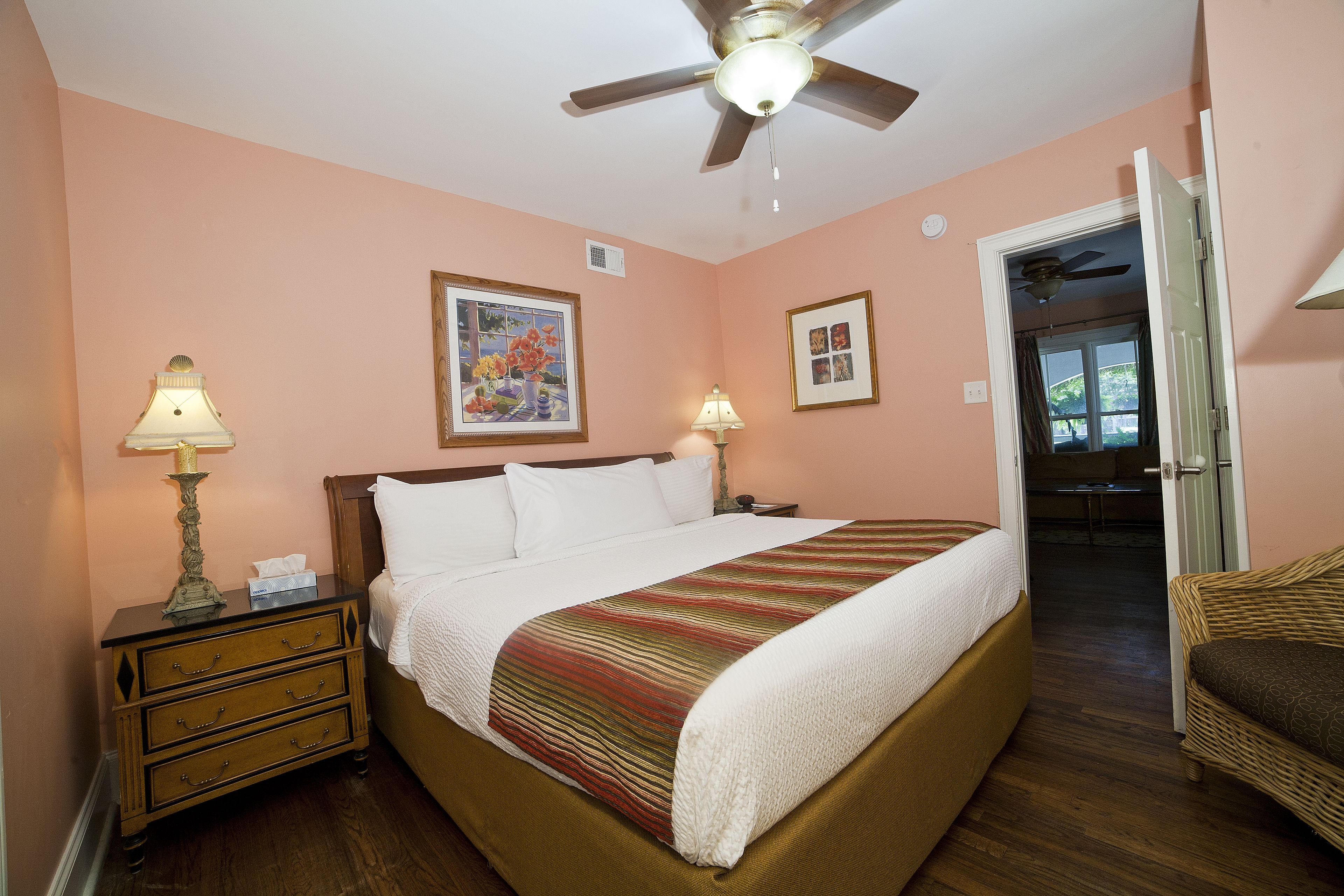 A bedroom with a bed, nightstands, a ceiling fan, and a door leading to another room.