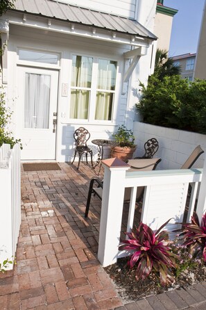 A patio with a white fence, a brick pathway, and outdoor furniture including a table and chairs.