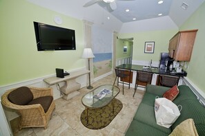 Una sala de estar con televisor, sofá, sillón, mesa de centro y una zona de cocina con refrigerador y pileta.