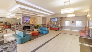 Eine großzügige Lobby mit Kamin aus Stein, blauen und roten Sofas, einer Küchenzeile und einem Essplatz.