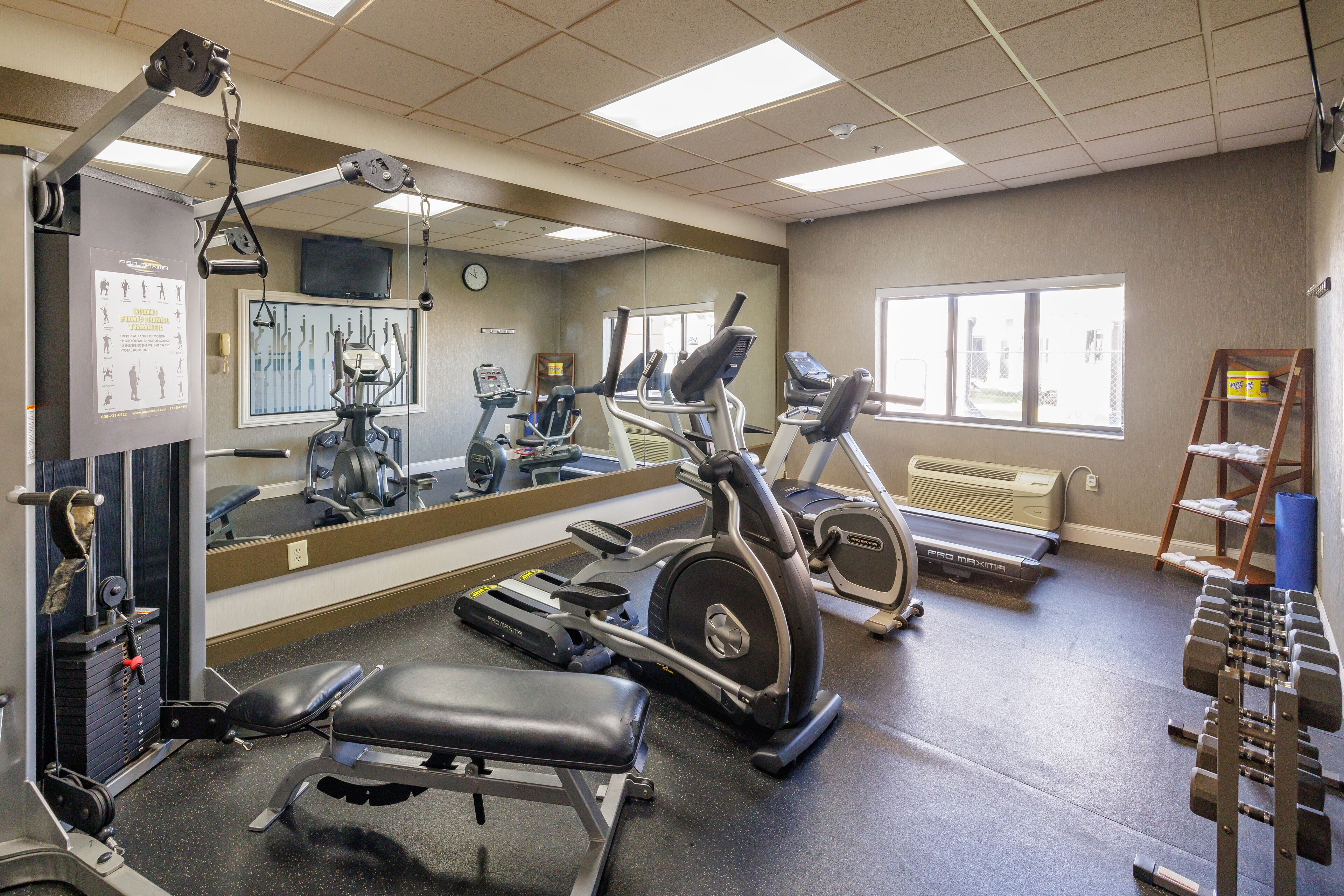 Uma academia com equipamentos de cardio, bancos de musculação e um espelho.