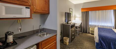 A hotel room with a kitchenette, a bed, a TV, and a window with curtains.