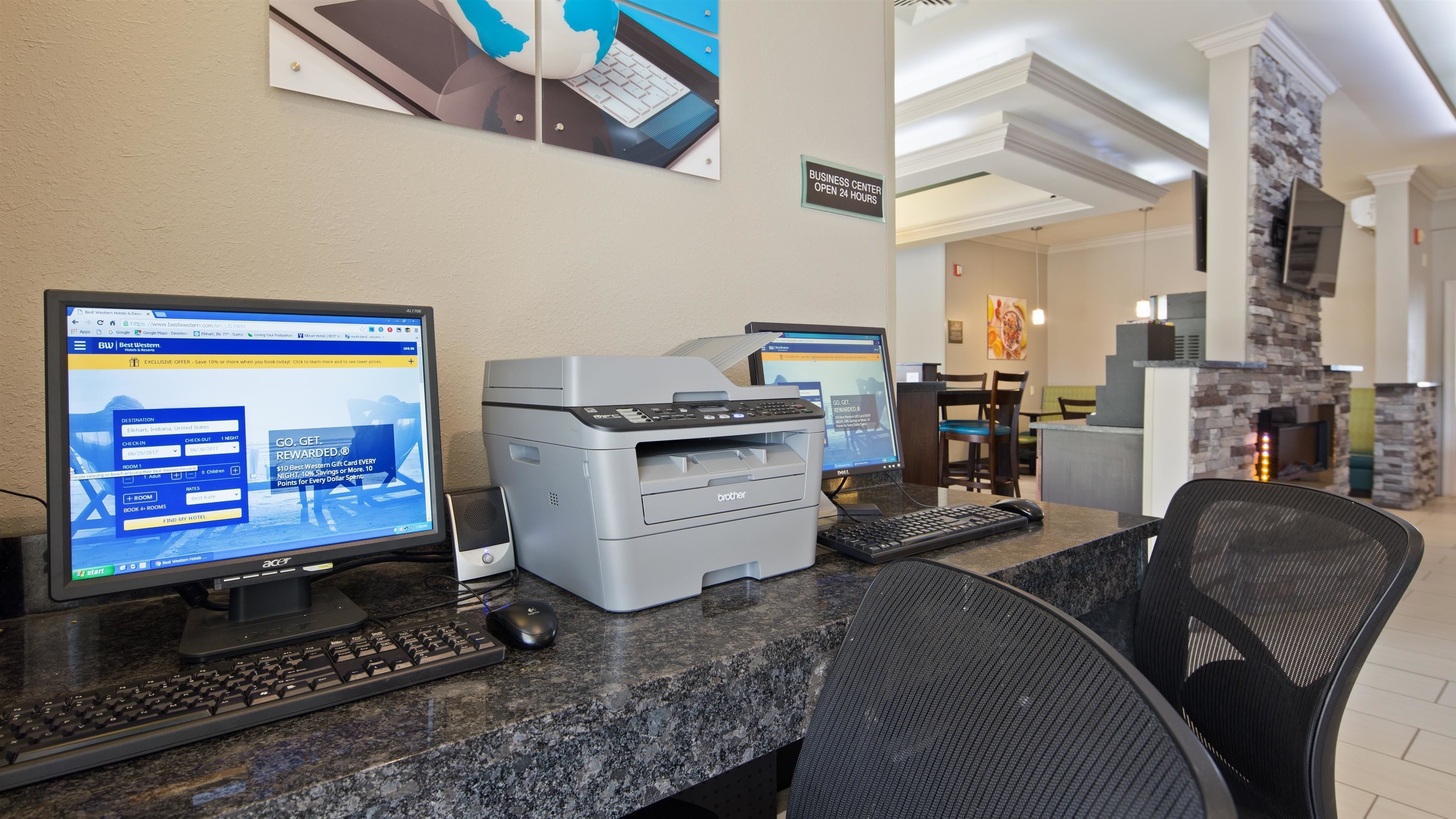 A hotel reception area with two computer monitors, a printer, a keyboard, and a mouse on a granite counter.