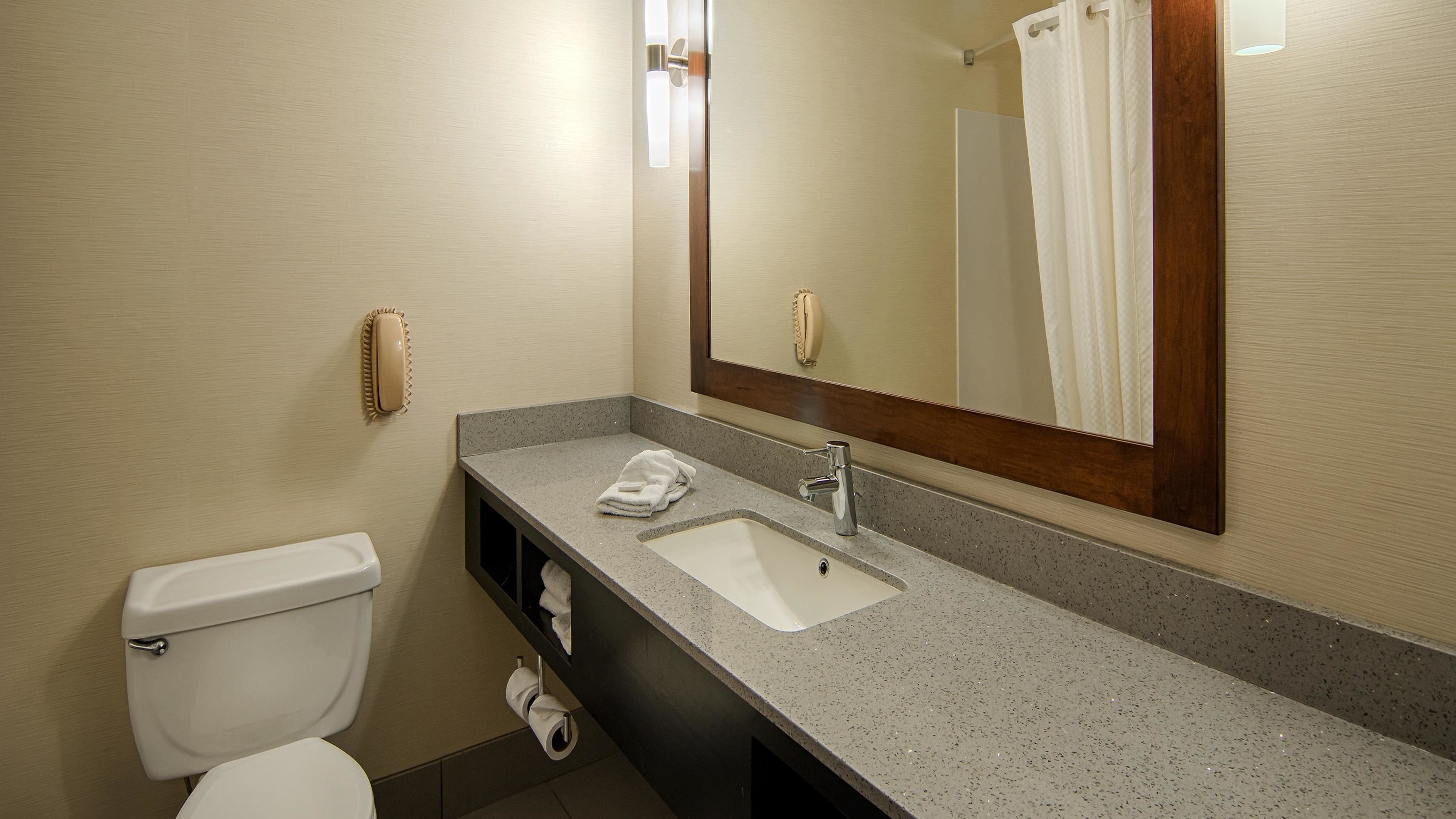 A bathroom with a toilet, sink, mirror, and towel rack.