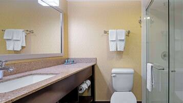 A bathroom with a granite countertop sink, a toilet, a glass-enclosed shower, and towels hanging on towel bars.