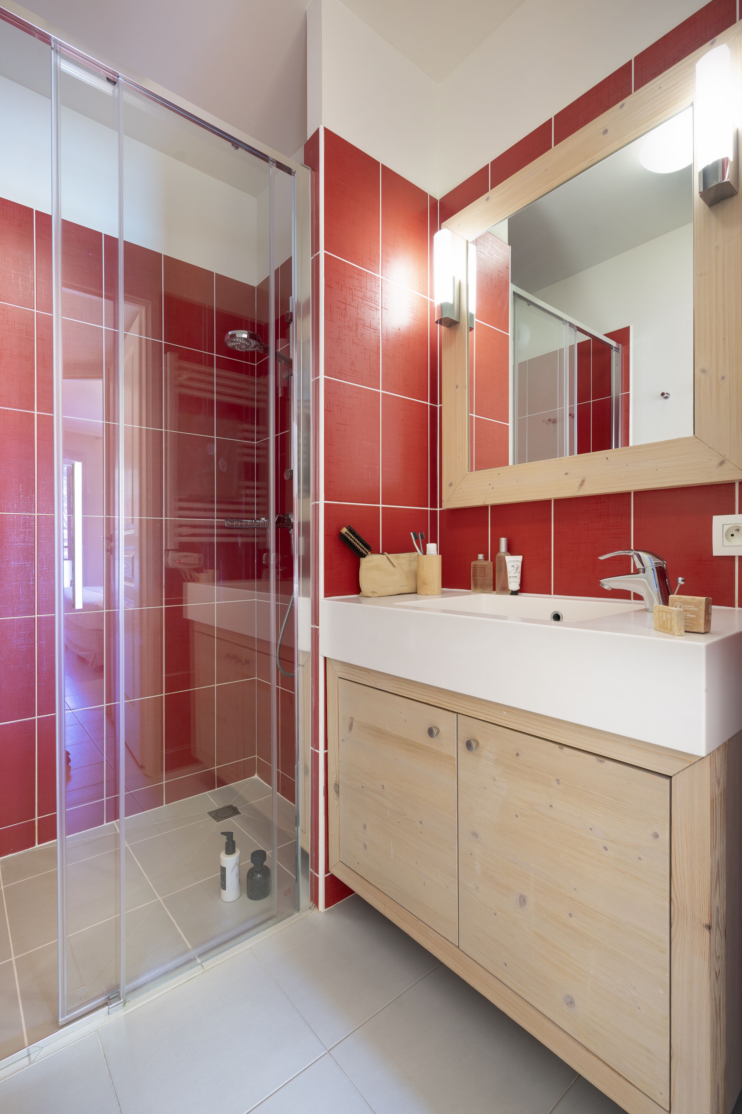 A bathroom with a glass-enclosed shower, a wooden vanity with a white sink, and red-tiled walls.