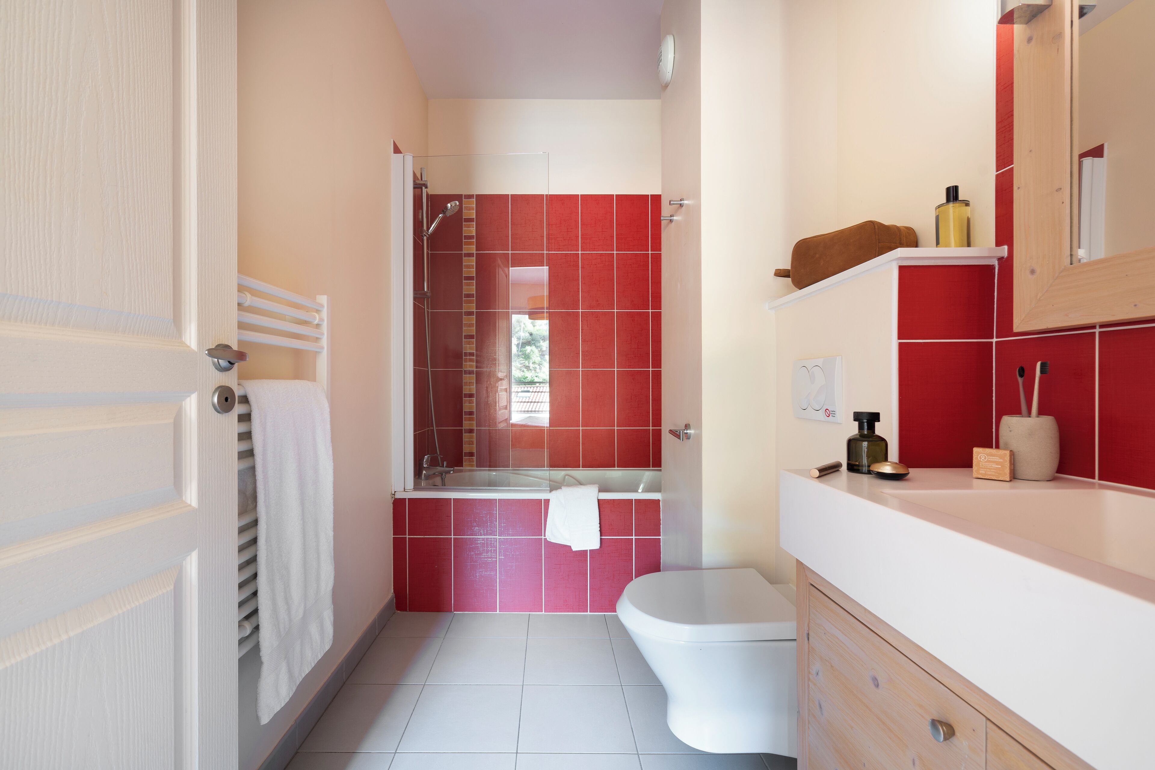 Une salle de bain avec des toilettes blanches, une douche en verre et un mur recouvert de carreaux rouges.