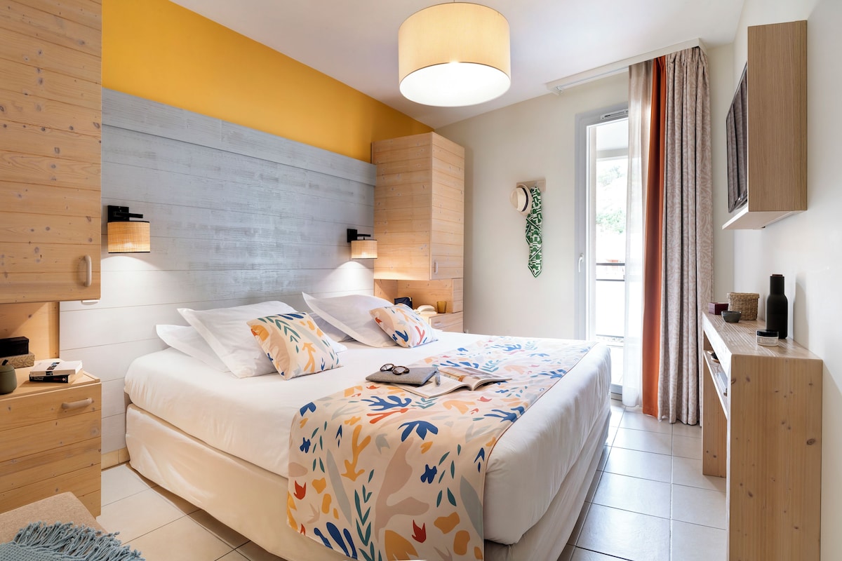 Un dormitorio moderno con cabecera de madera, una cama grande con ropa de cama estampada, lámparas de noche y vistas al exterior.