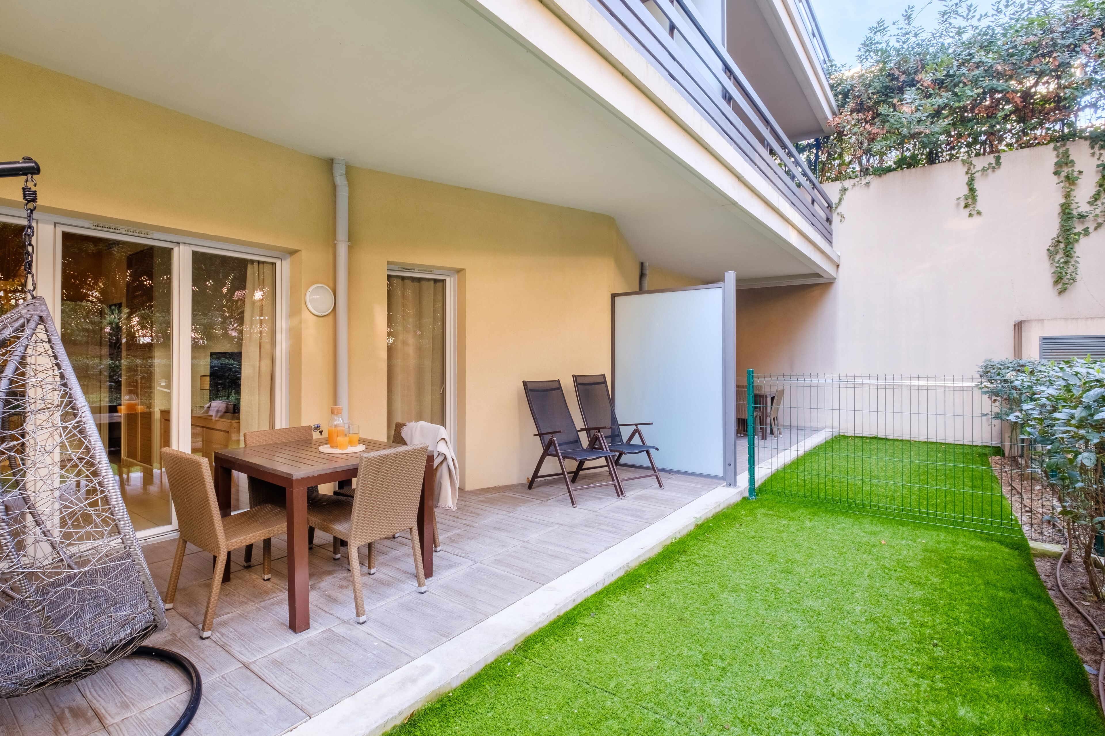 Une terrasse avec une table et des chaises, un fauteuil suspendu, un petit jardin et un tableau blanc.