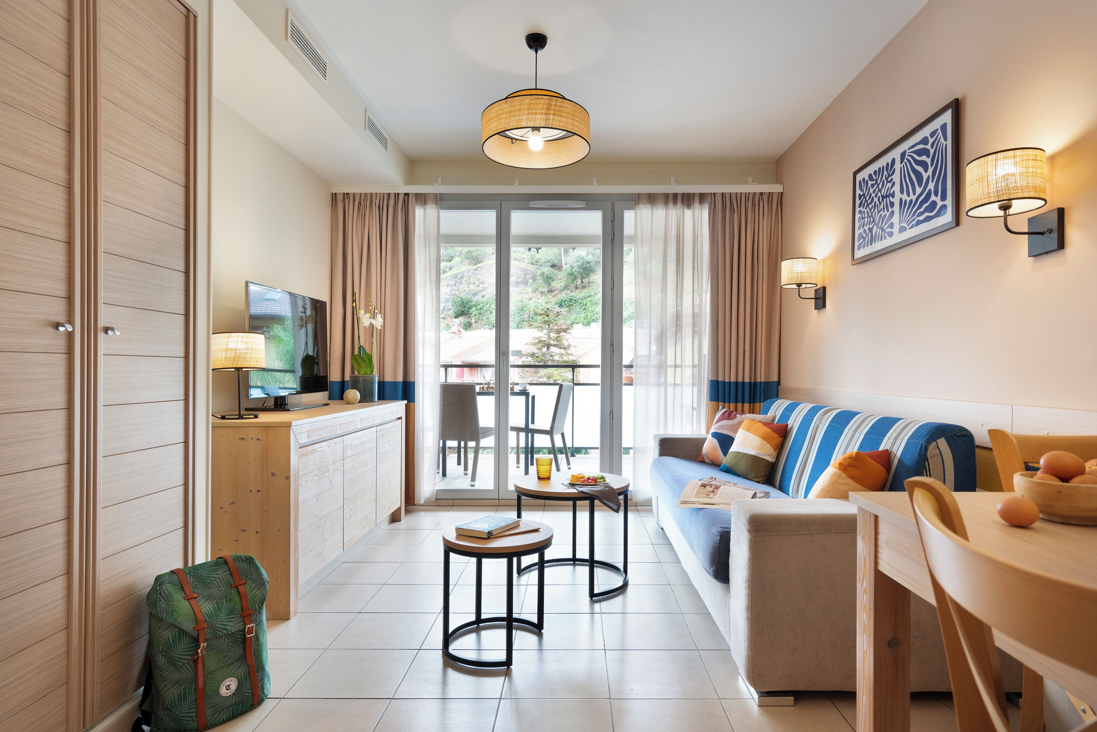 A hotel room with a sofa, a dining table, a TV, and a view of the outdoors.
