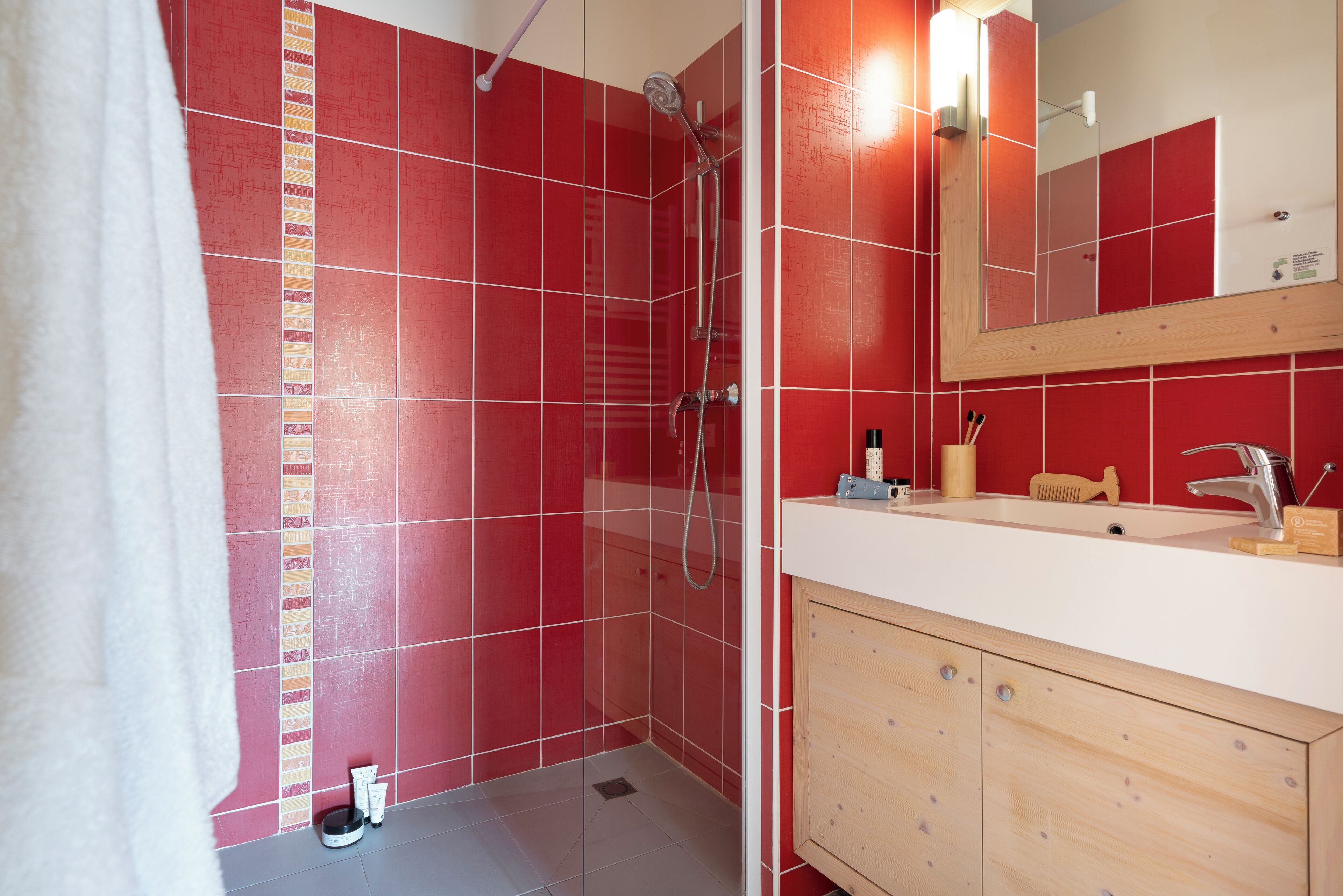 Une salle de bain avec des murs recouverts de carreaux rouges, une douche, un lavabo avec un miroir et des meubles en bois.