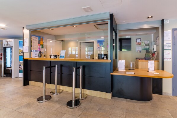 A reception area with a counter, two metal stanchions, and a sign for snacks and drinks. - Pierre & Vacances Residence Premium Julia Augusta (Roquebrune-Cap-Martin)