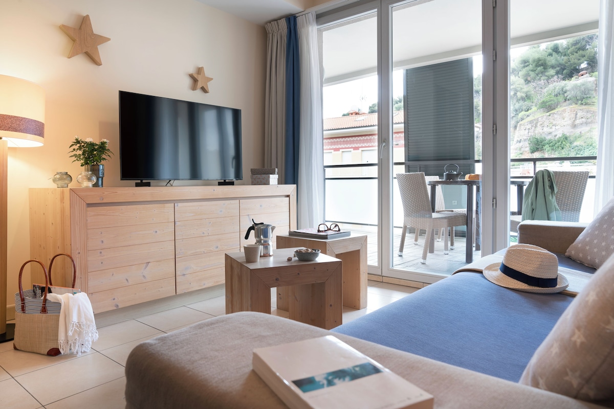 Habitación de hotel moderna con televisión de pantalla plana, muebles de madera, un balcón con mesa y sillas, y un ventanal con vistas al exterior.