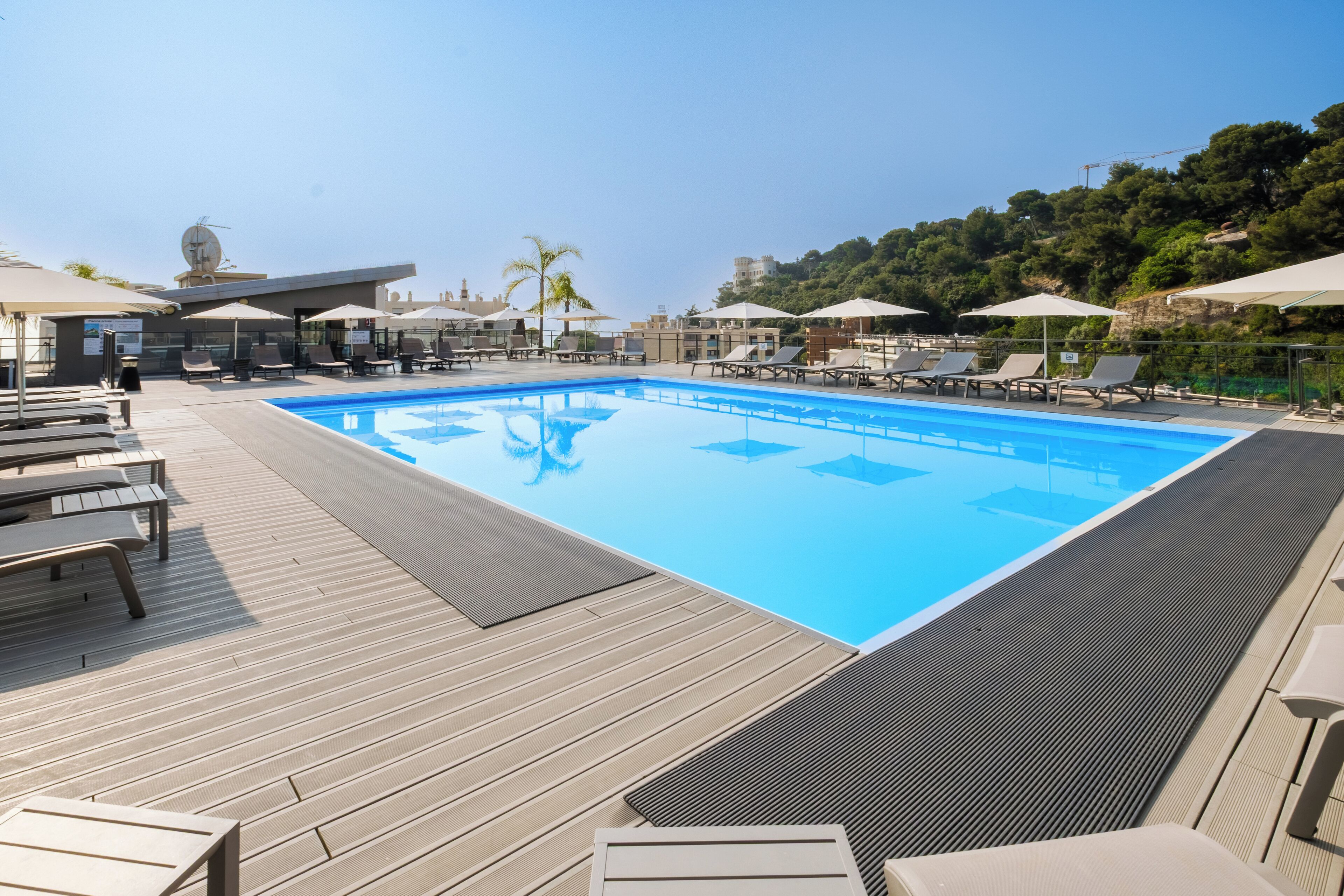 A pool area with lounge chairs and umbrellas, surrounded by a wooden deck and overlooking a hillside.