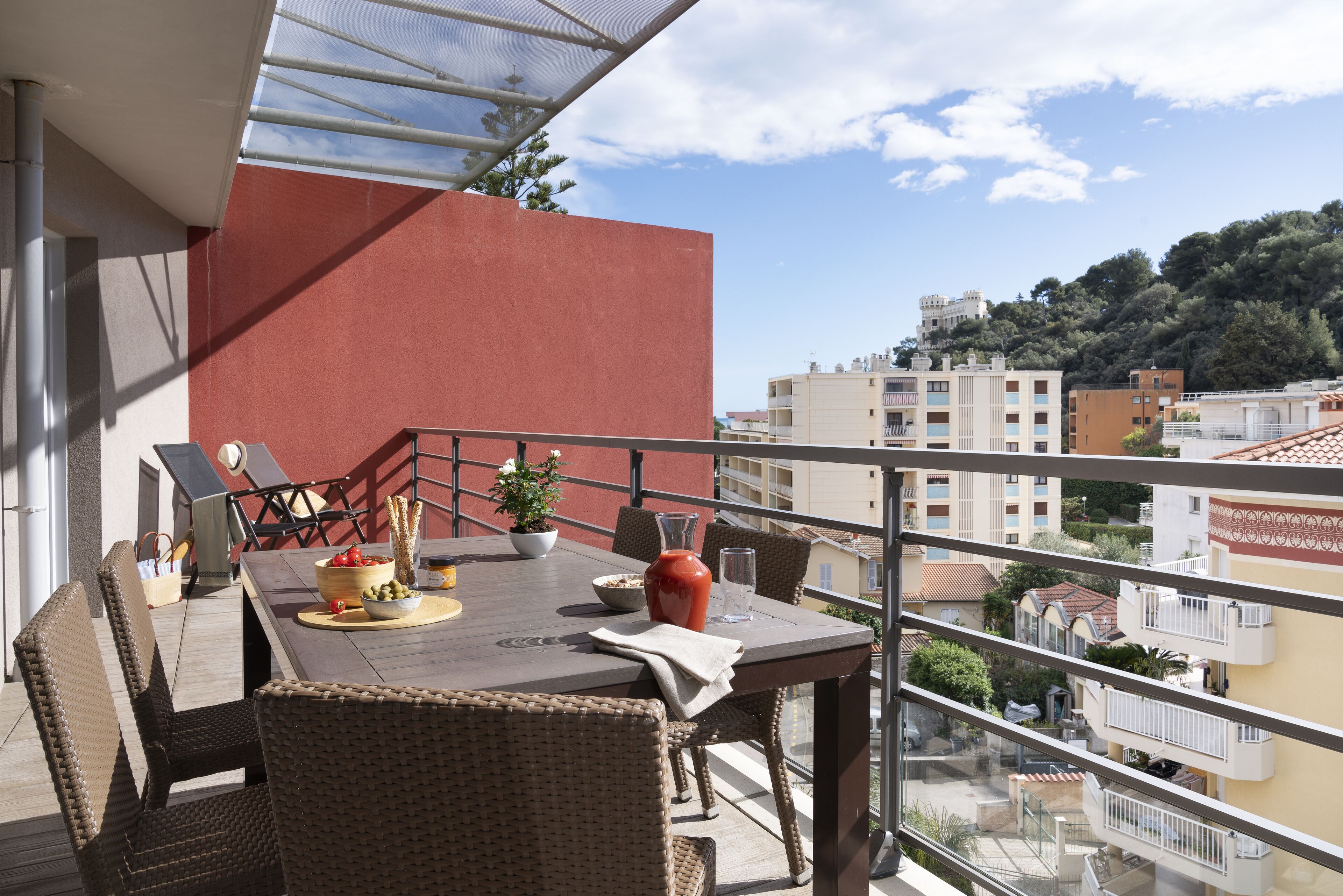 A balcony with wicker furniture, a table with a bowl of fruit, and a potted plant.
