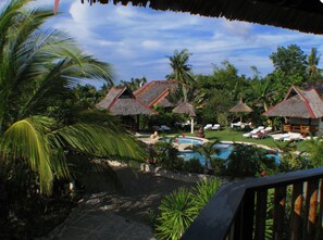 A resort with thatched-roof huts, a swimming pool, and lush tropical vegetation. - Dolphin House (Moalboal)