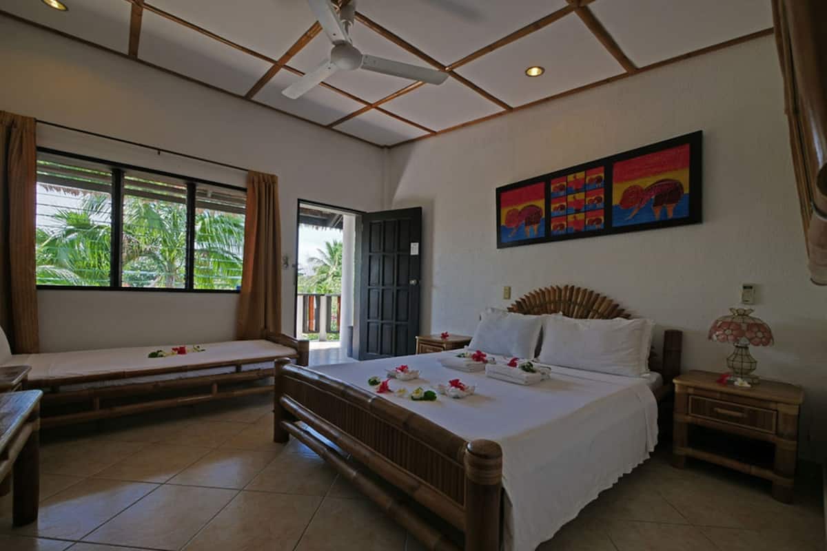 A hotel room with a large bed, a smaller bed, a ceiling fan, a window with curtains, and a painting on the wall.