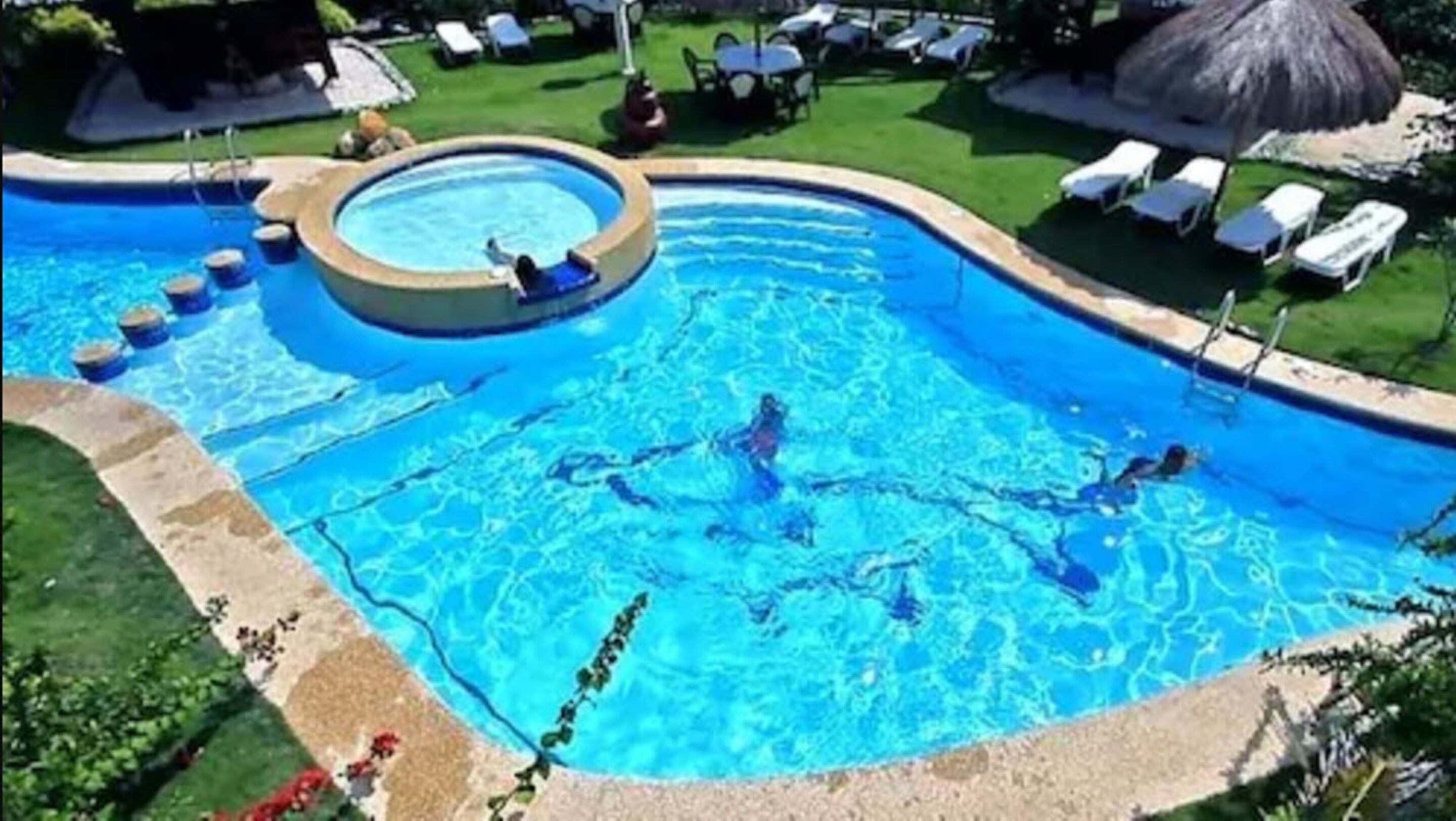 A swimming pool with a hot tub, surrounded by lounge chairs and a grassy area.