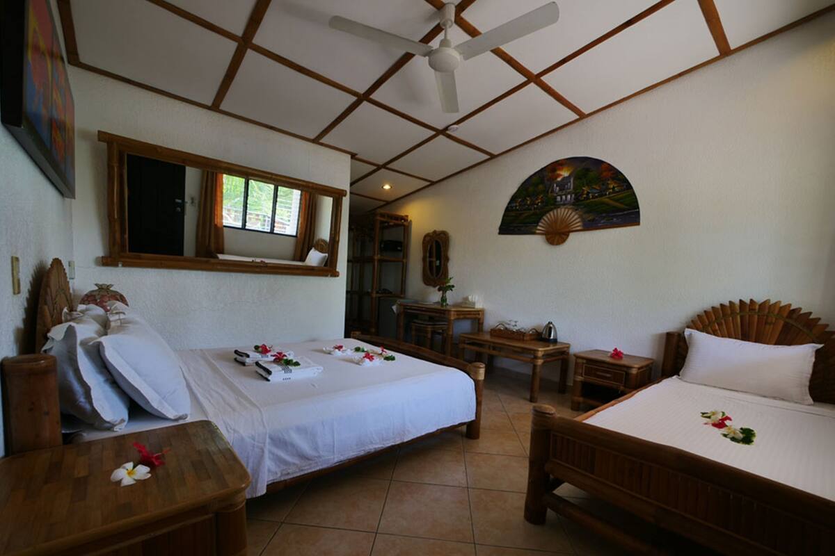 A hotel room with two beds, a ceiling fan, a desk, and a chair.