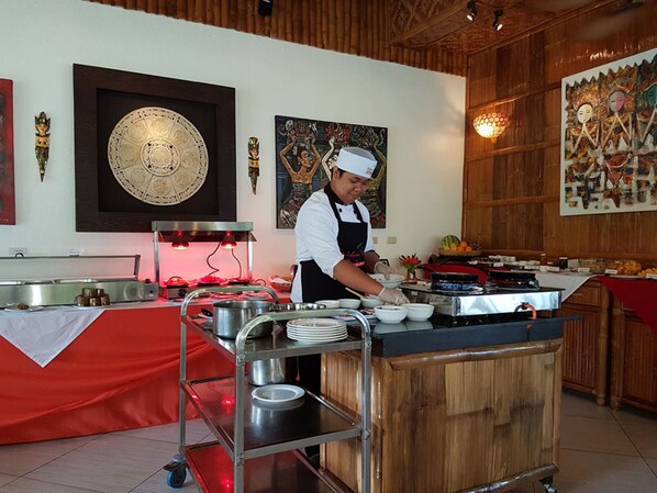 A kitchen area with a chef preparing food, a buffet table, and various kitchen equipment.
