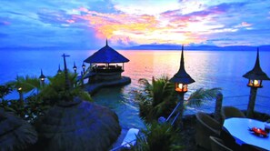 A sunset view over a calm sea with a small island structure featuring a gazebo and lanterns. - Dolphin House (Moalboal)