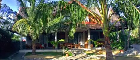 A tropical resort with palm trees, a thatched-roof building, and a paved walkway.