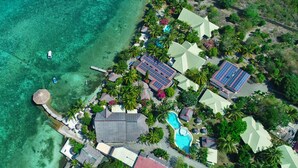 An aerial view of a resort with clear turquoise waters, a swimming pool, and several buildings with solar panels.