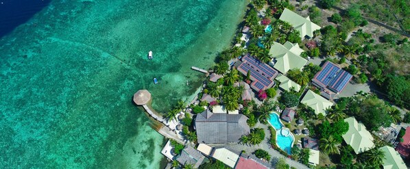 An aerial view of a resort with clear turquoise waters, a swimming pool, and several buildings with solar panels. - Dolphin House (Moalboal)