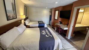 Ein Hotelzimmer mit zwei Betten, einem Schreibtisch, einem Stuhl, einem Fernseher und einem Badezimmer.