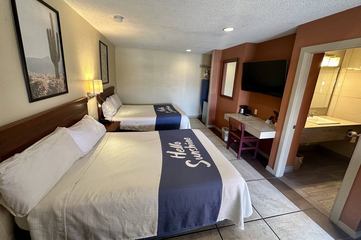 A hotel room with two beds, a desk, a chair, a television, and a bathroom.