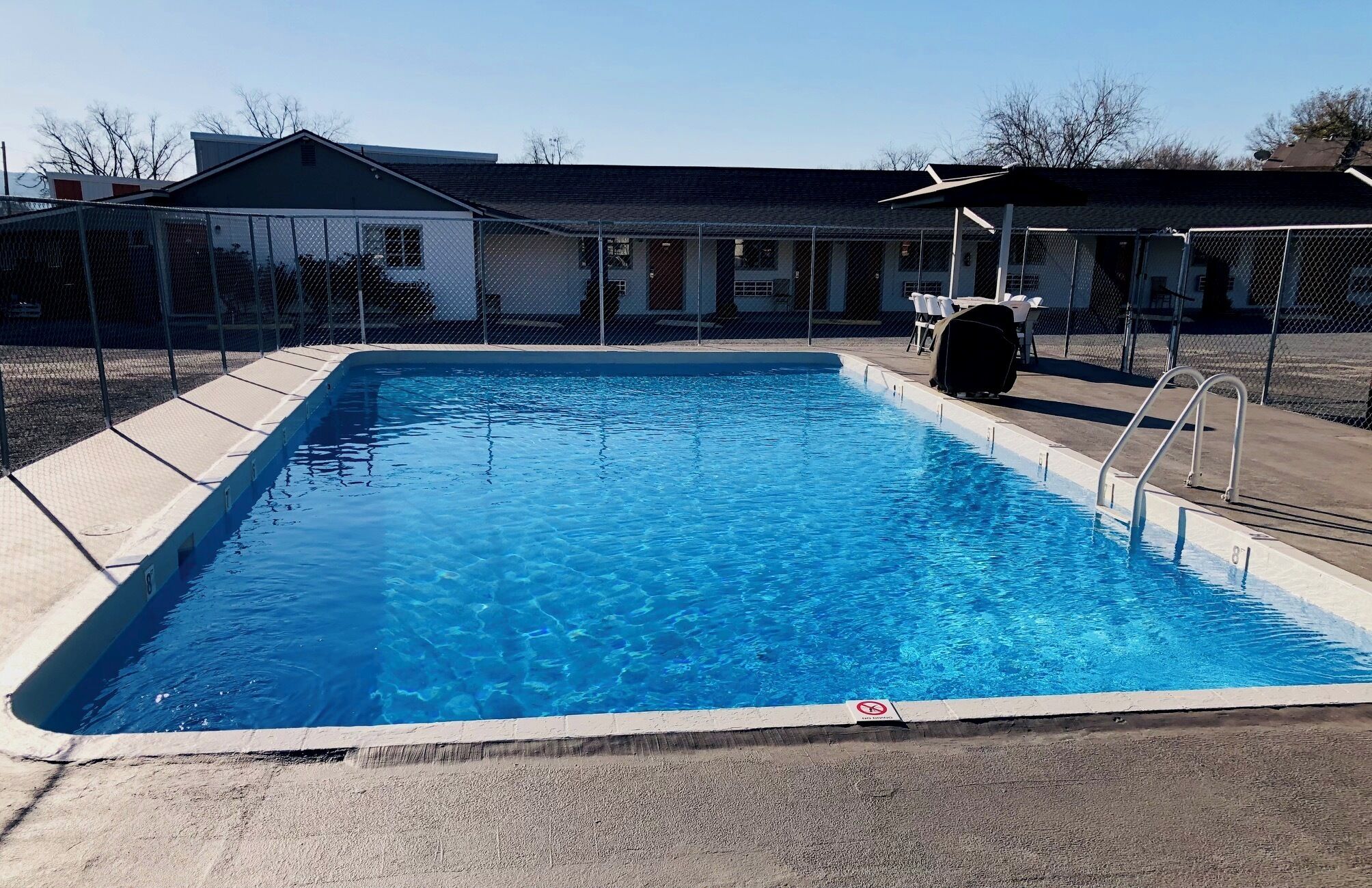 A rectangular swimming pool with clear blue water, surrounded by a concrete deck.