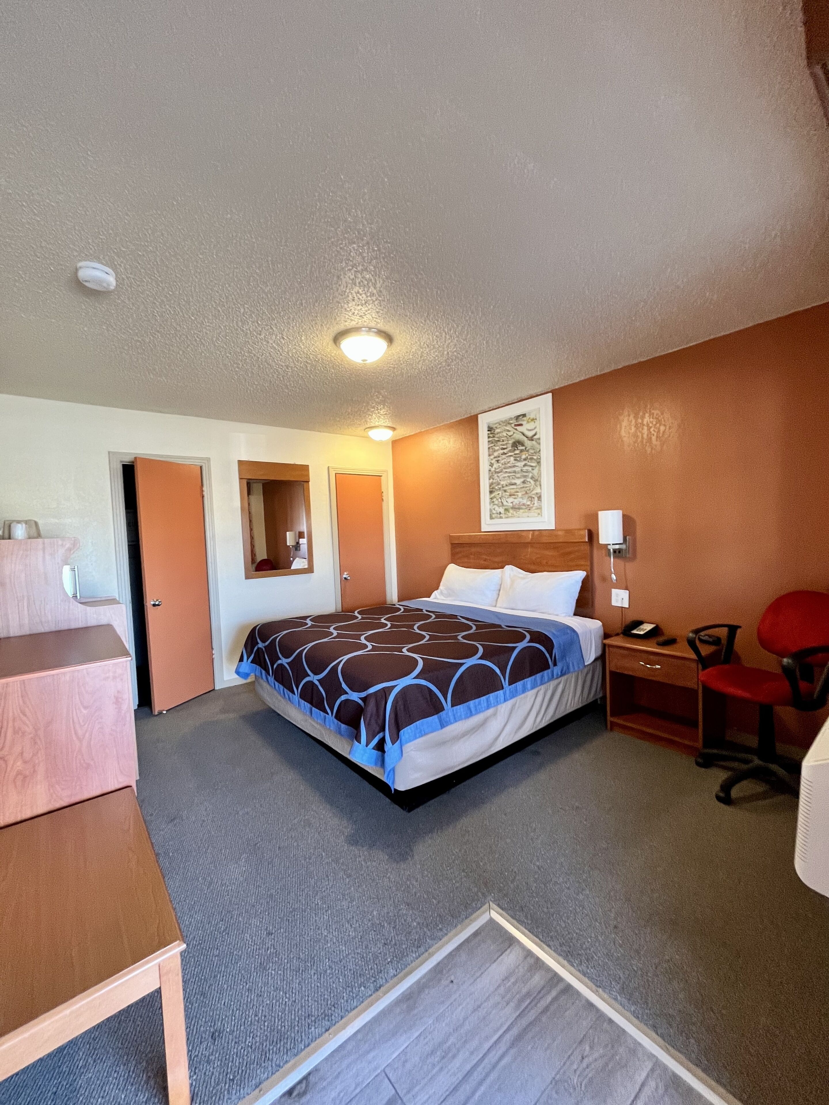 Una habitación de hotel con cama, escritorio, silla y cómoda.