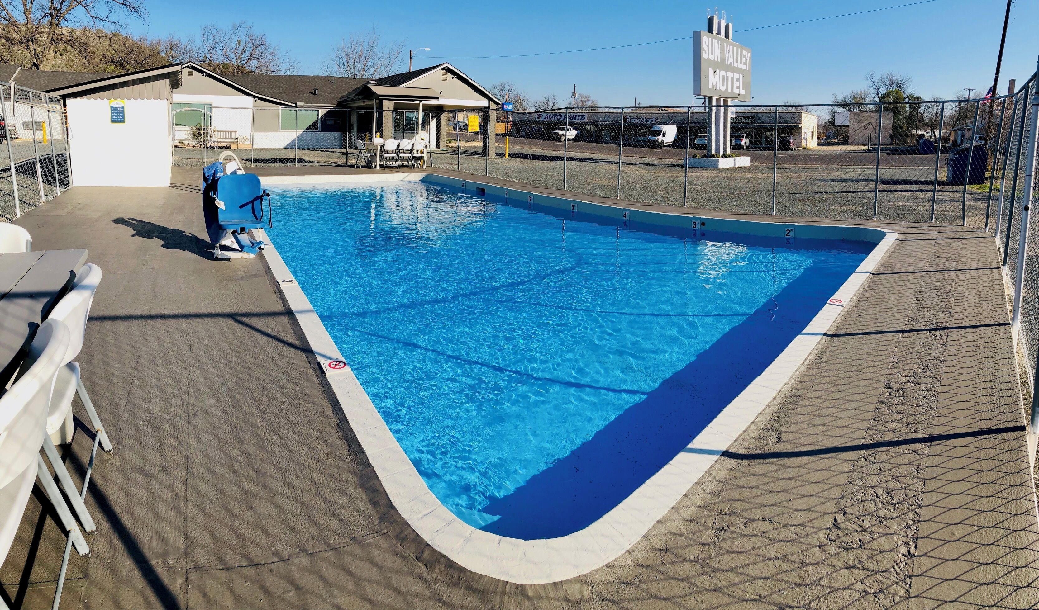 A swimming pool with numbered lanes, a covered seating area, and a fenced parking lot.