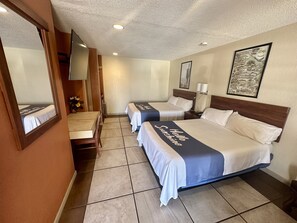 A hotel room with two beds, a desk, a chair, a mirror, a TV, and a framed picture on the wall.