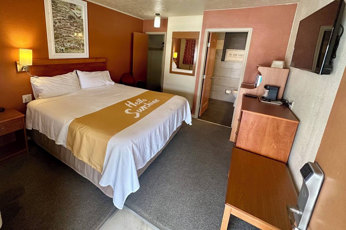 A hotel room with a bed, a desk, a mirror, and a door leading to a bathroom.