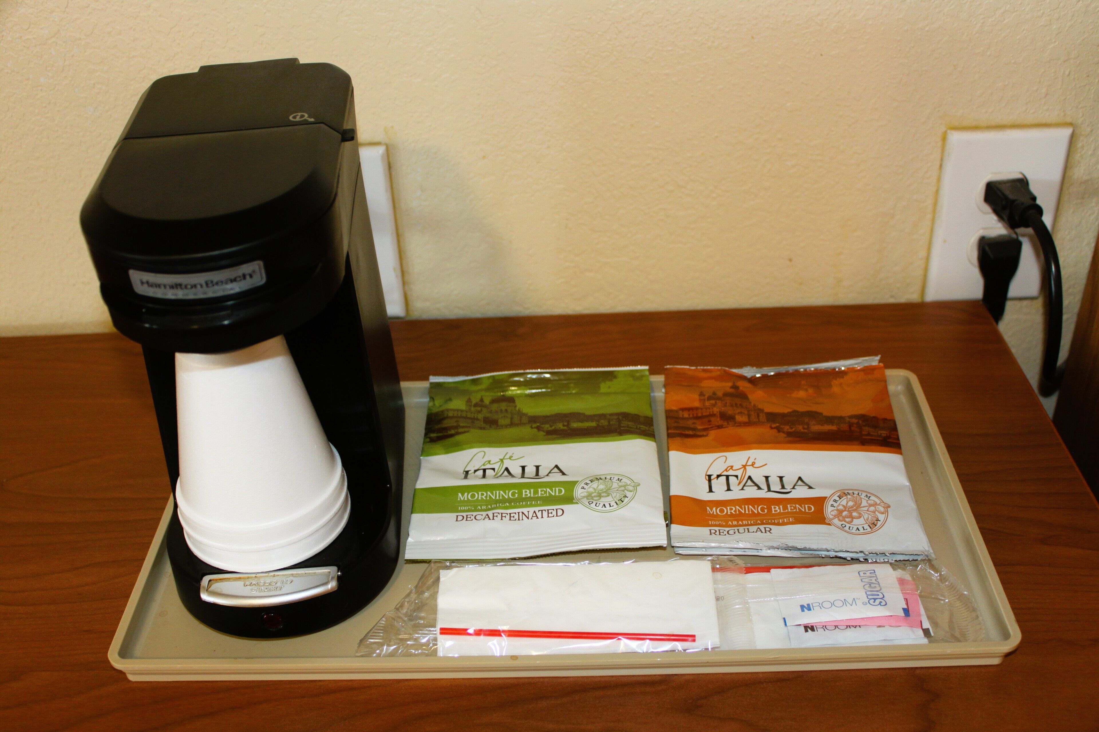 Eine Kaffeemaschine, zwei Packungen entkoffeinierten Kaffees und einige Pflegeprodukte auf einem Tablett.