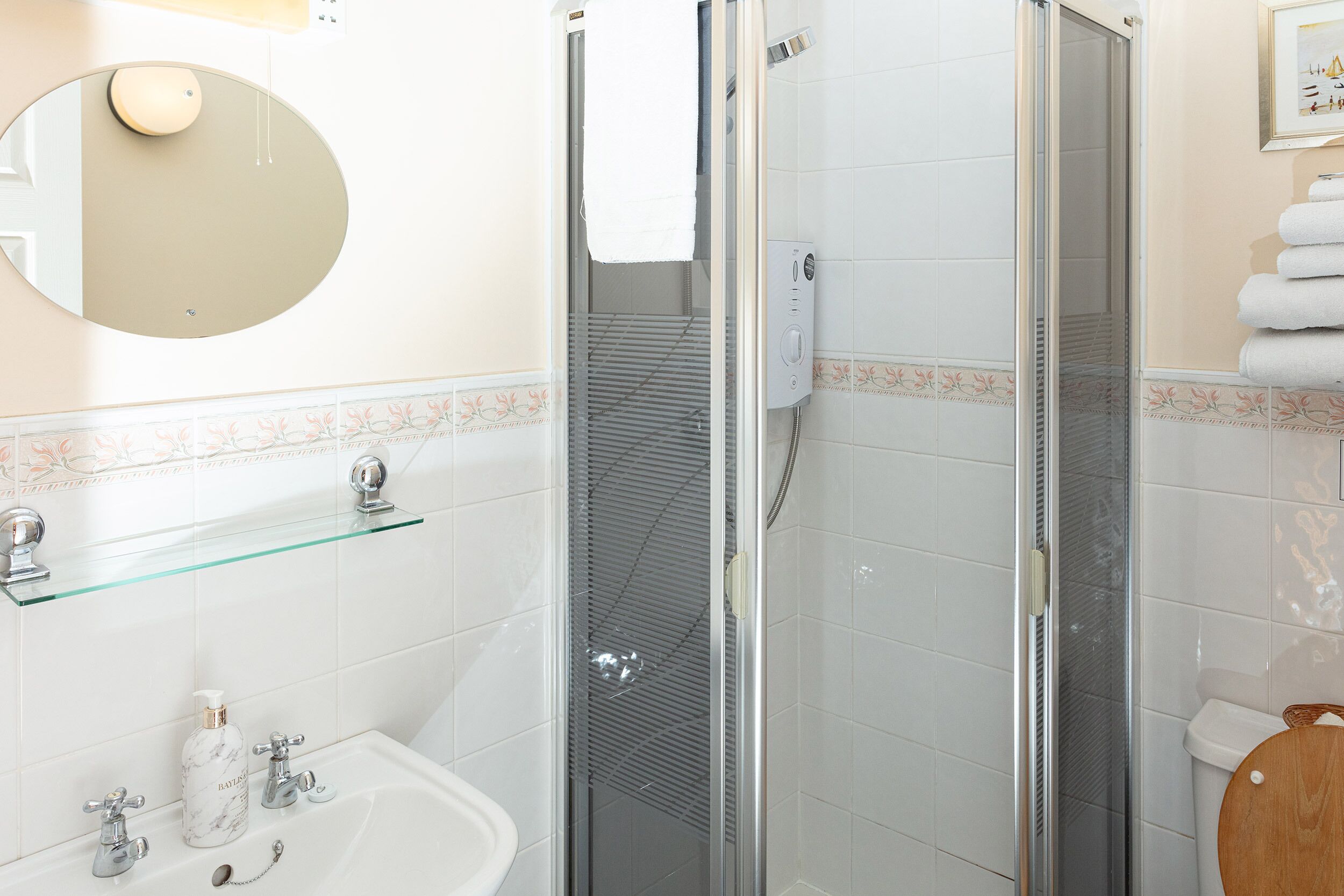 A bathroom with a glass-enclosed shower, a sink with two faucets, a mirror, and a towel rack with folded towels.