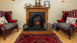 Una sala de estar acogedora con chimenea, dos sillones de cuero, un tapete estampado rojo y apliques de pared.