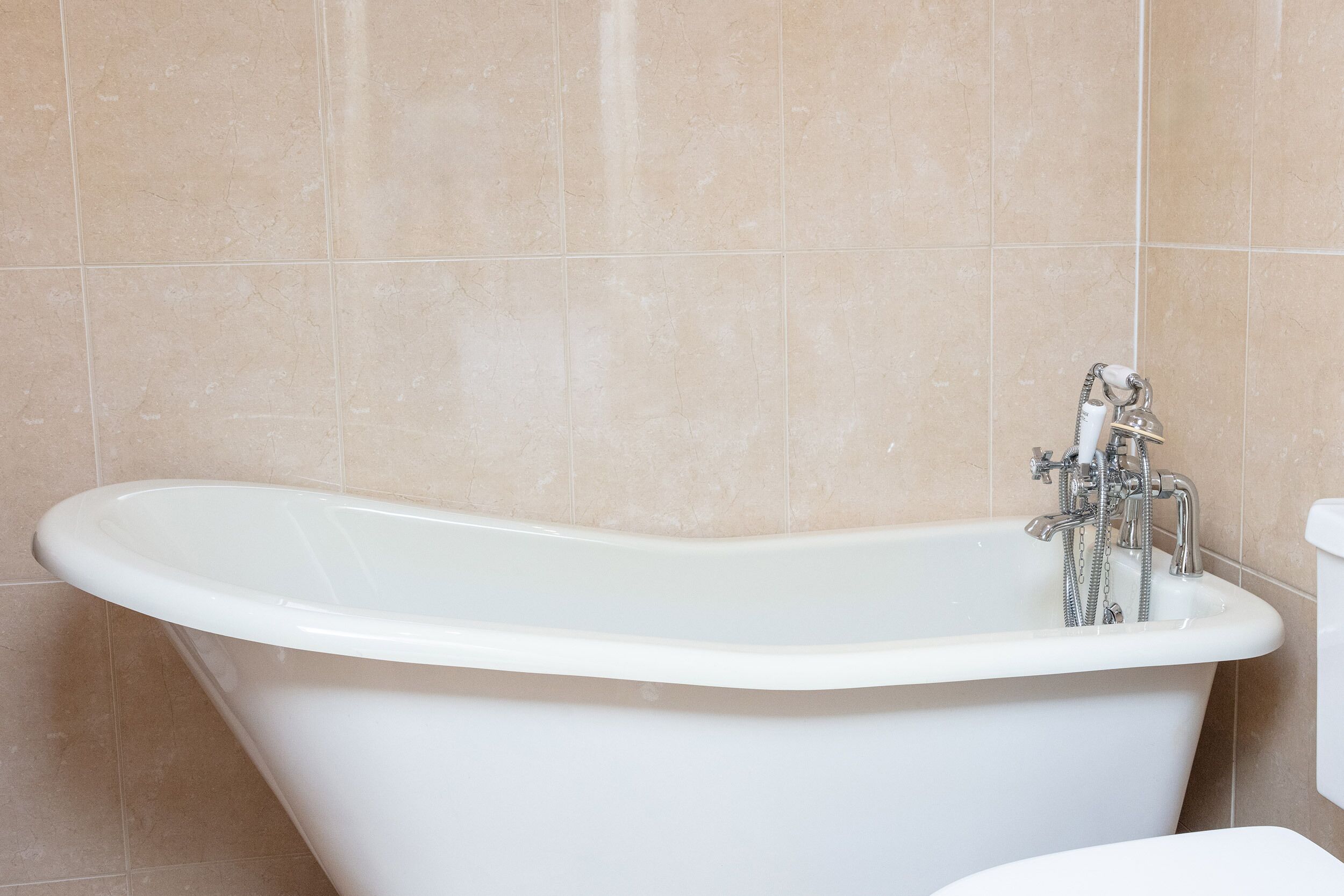 Eine weiße, freistehende Badewanne in einem Badezimmer mit beige gefliesten Wänden.