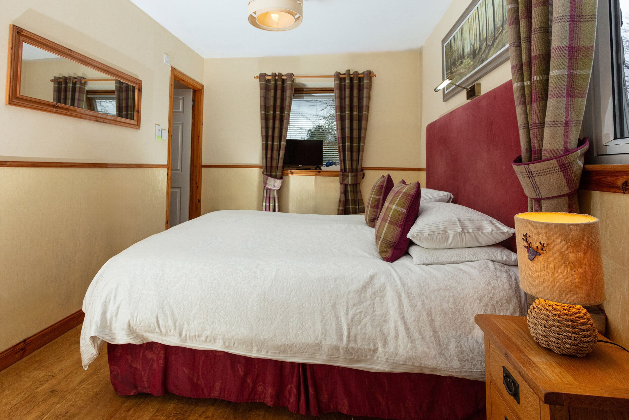 A bedroom with a large bed, a wooden headboard, a bedside lamp, and plaid curtains.