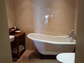 Un baño con bañera independiente, inodoro y tocador de madera con lavamanos.