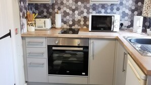 Een compacte keuken met een magnetron, toaster en oven. Er is een backsplash van hexagontegels en een klok aan de muur.