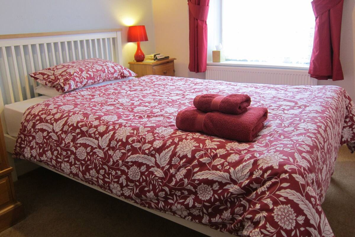 Una cama bien hecha con una colcha estampada de flores y dos toallas enrolladas encima.
